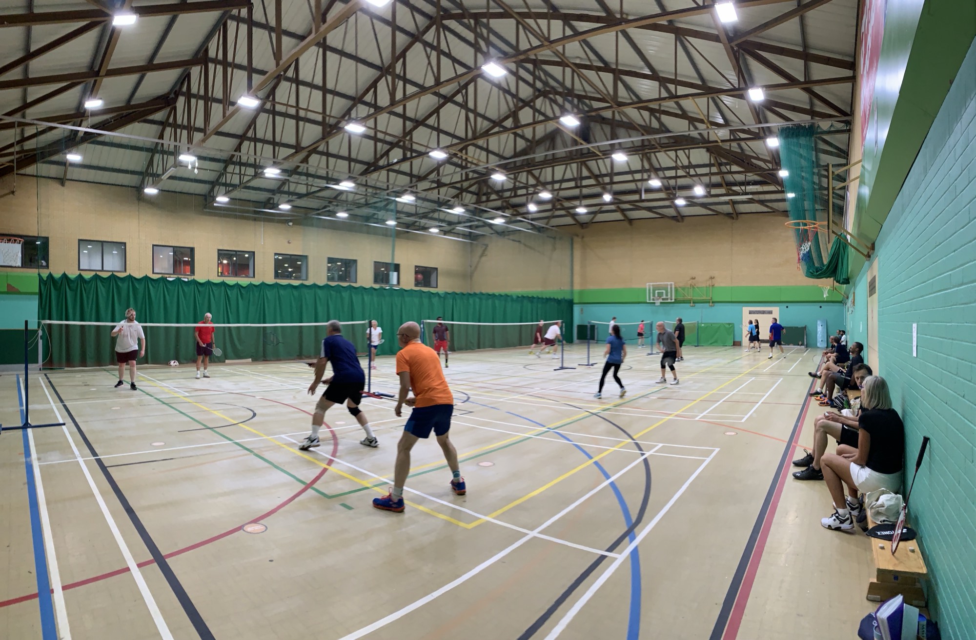 A busy Dorset sports hall with adults playing badminton across several courts